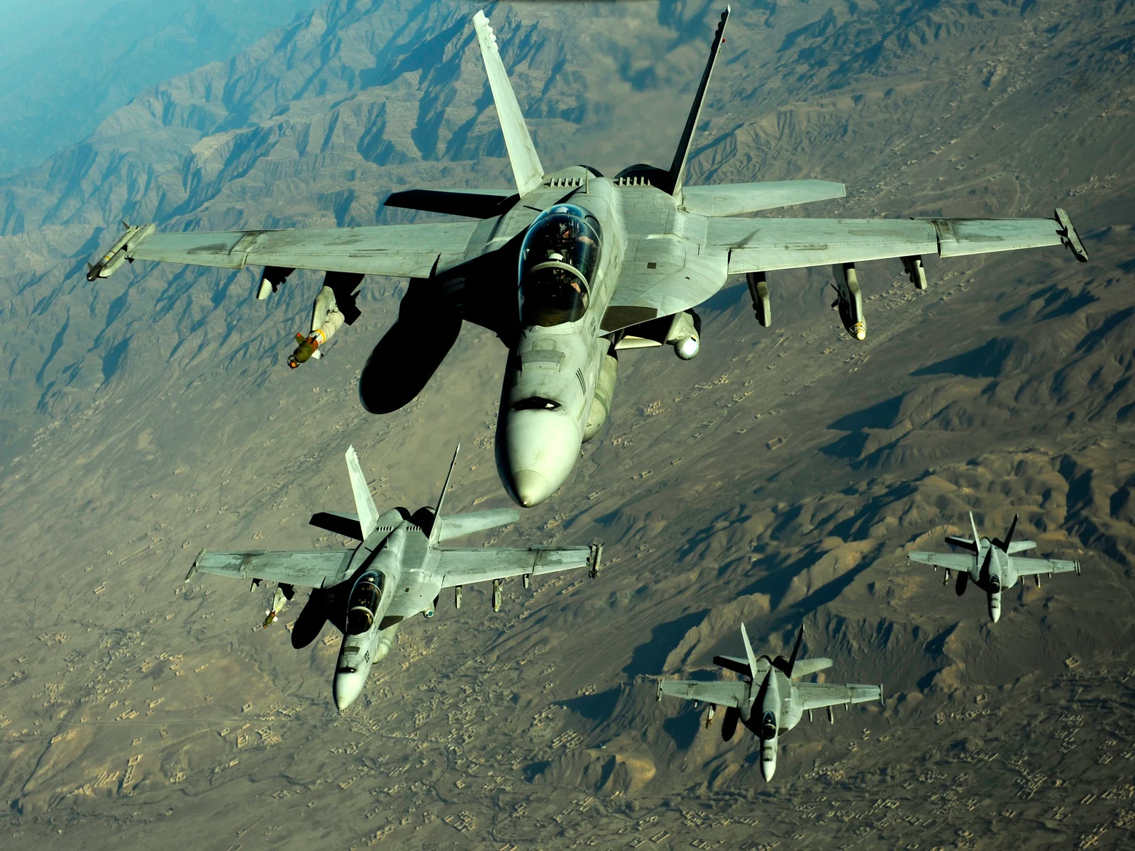 Four U.S. Navy F/A-18 aircraft flying over mountains in Afghanistan during a 2010 mission